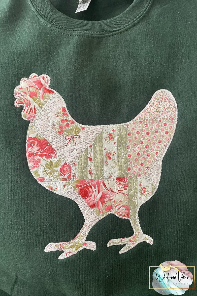 A dark green sweatshirt with an appliqued chicken. The chicken is made of a printed patchwork fabric with pink and green floral patterns. The text 'Weekend Vibes Apparel' is printed in white on a pink background in the lower right corner of the image.
