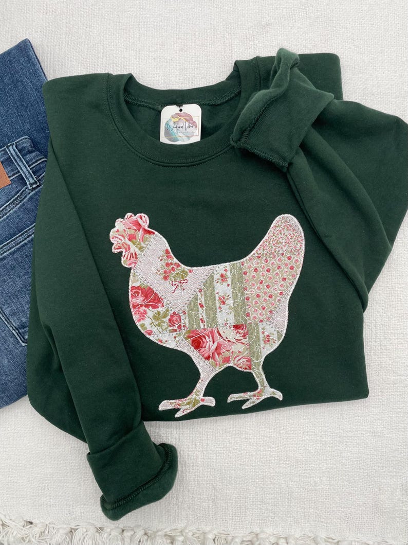 Appliquéd chicken on green sweatshirt. Chicken is appliquéd using a patchwork printed fabric of sage green and pinks on a white background. The appliquéd fabric has a white zigzag thread border and white stippling.