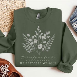 May include: A green sweatshirt with a floral design and the text "He leads me beside still waters HE RESTORES MY SOUL".
