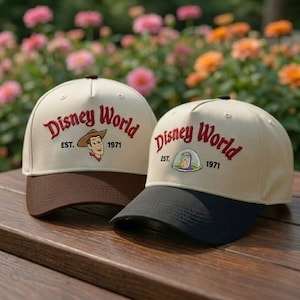 May include: Two baseball caps with the text "Disney World" in red script, with "EST. 1971" below. One cap has a brown brim and Woody from Toy Story, the other has a black brim and Buzz Lightyear.