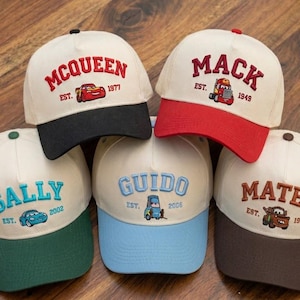 Può includere: Cinque cappellini da baseball con testo ricamato e grafica di auto dei cartoni animati. I cappellini presentano i nomi "McQueen", "Mack", "Sally", "Guido" e "Mater". Ogni cappellino ha una diversa combinazione di colori, tra cui visiere nere, rosse, verdi, blu e marroni.