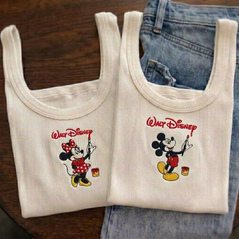 May include: Two off-white ribbed tank tops with the "Walt Disney" logo in red. One tank top features Minnie Mouse in a red polka dot dress, and the other features Mickey Mouse. Both are holding paintbrushes and standing next to paint cans.