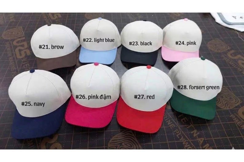 May include: A collection of baseball caps with white crowns and colored brims. The caps are labeled with numbers and colors, including brown, light blue, black, pink, navy, pink, red, and forest green.