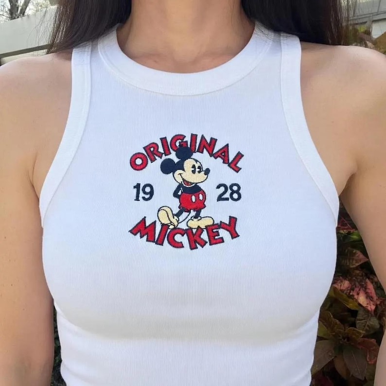 May include: White ribbed vest top with a Mickey Mouse graphic. The design includes the word "ORIGINAL" in red, the numbers "19" and "28", and the word "MICKEY" in red. The vest top has a round neckline and a sleeveless design.