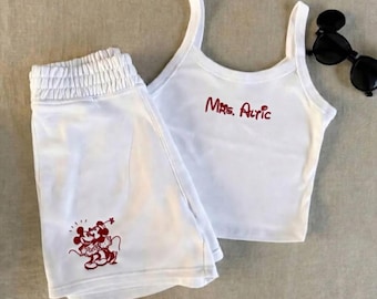 May include: White two-piece sleepwear set. The set includes a tank top with the text "Mrs. Alric" in red script and matching shorts with a red cartoon graphic. Black sunglasses with Mickey Mouse ears are also present.