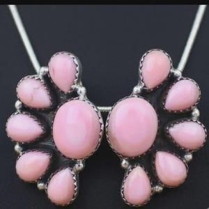 May include: A pair of silver-toned earrings with a cluster of pink gemstones. Each earring features a central oval stone surrounded by smaller, teardrop-shaped stones. The earrings are suspended from a silver chain.