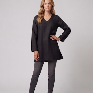 May include: A woman wearing a dark gray tunic with a V-neck and long sleeves, paired with gray skinny jeans and brown ankle boots. The tunic has a slightly flared hem. The background is a plain light gray.