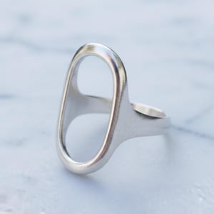 May include: A silver ring with an elongated oval design. The ring features a smooth, polished finish and a minimalist aesthetic. The open oval shape creates a modern and unique look, suitable for everyday wear.
