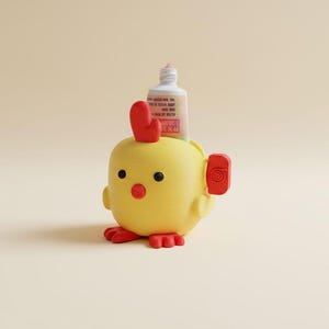Puede incluir: Un exprimidor de tubos con forma de pollito amarillo con cresta, pico y patas rojas. El soporte cuenta con una pequeña manivela lateral roja y contiene un tubo blanco de crema con texto visible, diseñado para ayudar a extraer el contenido del tubo.