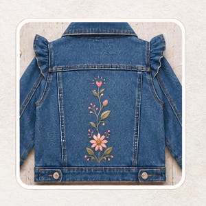 Puede incluir: Una chaqueta de mezclilla azul con una superficie de tela texturizada, cuello y detalles de volantes en los hombros. El panel trasero muestra un diseño floral vertical central con hojas verdes, pétalos rosas y un pequeño corazón rosa.