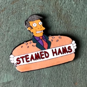 Op de afbeelding: Een cartoonfiguur uit The Simpsons, met bruin haar en een blauw pak, houdt een spandoek vast met de tekst "STEAMED HAMS". Het figuur bevindt zich in een broodje, wat een parodie is op een hotdog.