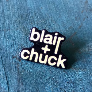 May include: Black enamel pin with white text that reads "blair + chuck".