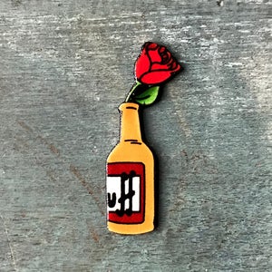May include: A yellow bottle with the word "DUFF" in red and white, topped with a red rose with green leaves. The image is set against a weathered, blue-gray background.