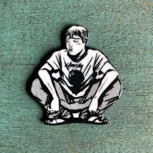 May include: Black and white illustration of a person sitting with their legs crossed, wearing a t-shirt with a black and white graphic of a bowling ball and the word "Sams" on it. The person is smoking a cigarette.