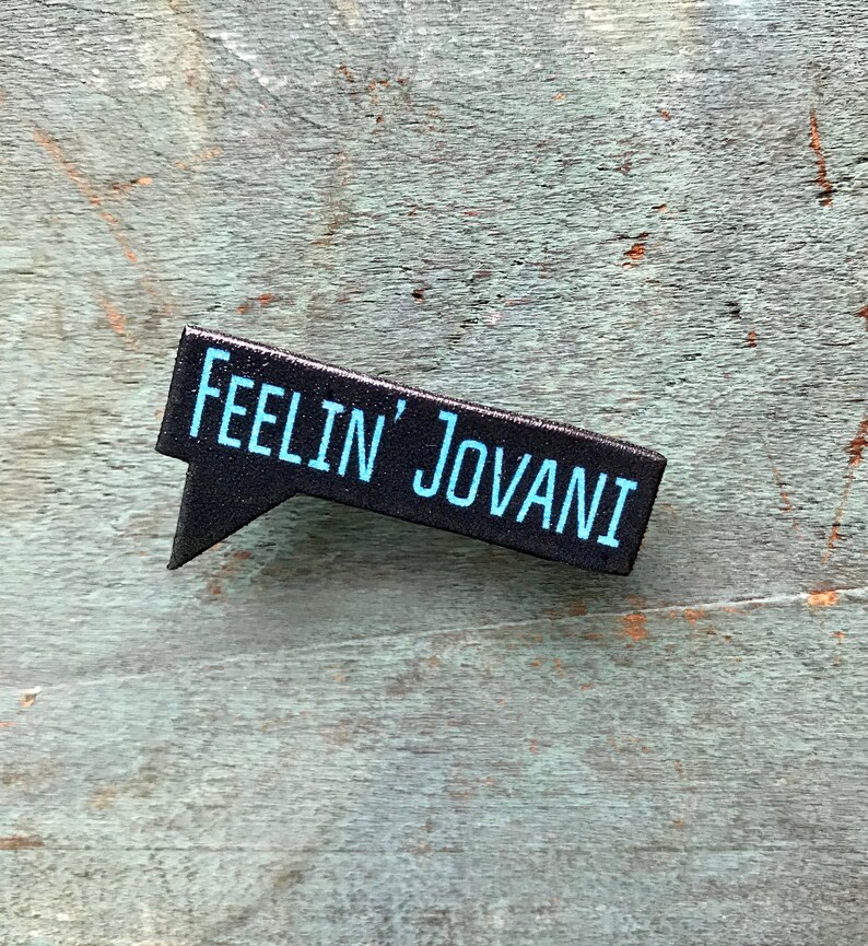 Puede incluir: Pin de burbuja de di&aacute;logo en blanco y negro con el texto "Feelin' Jovani" en azul.