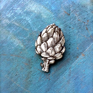 May include: A white wooden artichoke cutout on a blue background. The artichoke is detailed with lines and shading to give it a realistic look.