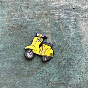 May include: A yellow wooden scooter with black wheels and a black number "1" on the side. The scooter is on a green wooden background.