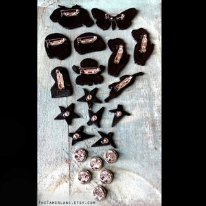 May include: A collection of 15 black and silver pins featuring various designs, including butterflies, stars, and abstract shapes. The pins are displayed on a wooden surface.