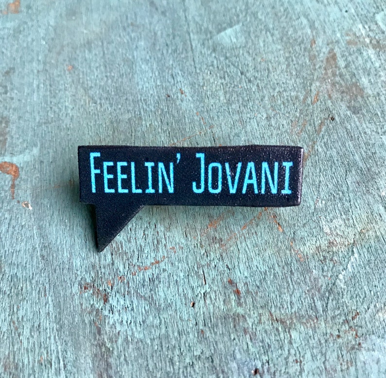 Puede incluir: Pin de burbuja de di&aacute;logo en blanco y negro con el texto "Feelin' Jovani" en azul.