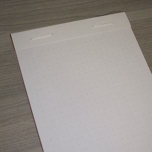 May include: A white notebook with a dotted grid pattern and two white strings at the top.
