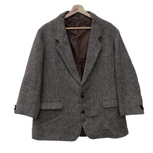 May include: A brown and black tweed blazer with a single-breasted closure and two button pockets. The blazer has a herringbone pattern and a brown lining.