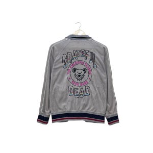 May include: Gray zip-up jacket with the text "Grateful Dead" and a bear graphic on the back. The jacket has white trim, a navy blue and red striped hem, and a collar. The text "The American Classic Rock Band" is also visible.