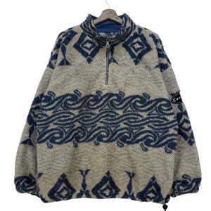 May include: A beige fleece pullover with a blue and white geometric pattern. The pullover has a half-zip closure and a high neck. The brand name "Esprit" is visible on the right sleeve.