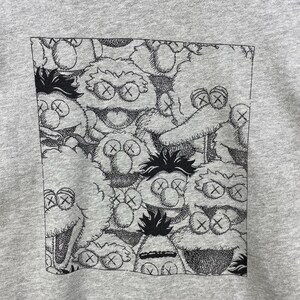 Peut inclure: Un sweat-shirt gris avec un motif noir et blanc de personnages de dessins anim&eacute;s aux yeux en forme de X. Le motif est contenu dans un rectangle noir. Les personnages ont des expressions vari&eacute;es et sont dens&eacute;ment regroup&eacute;s.
