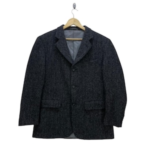 May include: A dark gray tweed blazer with a three-button closure, two front pockets, and a notched lapel. The jacket is hanging on a wooden hanger against a white background. The blazer has a gray lining.