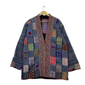 May include: A patchwork jacket with a V-neck design. The jacket features a variety of colorful embroidered patches in red, blue, green, and purple. The jacket is hanging on a wooden hanger against a white background.
