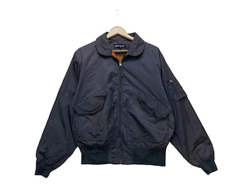 Puede incluir: Una chaqueta bomber gris oscuro con cierre de cremallera y un pequeño bolsillo en la manga izquierda. La chaqueta tiene una etiqueta negra con el texto "D'REX" en el interior del cuello.