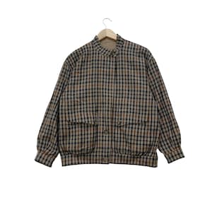 May include: A brown, black, and tan plaid jacket with two front pockets and a button closure. The jacket is hanging on a wooden hanger against a white background. The jacket has long sleeves and a round collar.