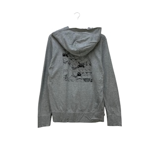Peut inclure: Un sweat &agrave; capuche gris zipp&eacute; avec une capuche. Le dos du sweat &agrave; capuche pr&eacute;sente une impression graphique en noir et blanc de personnages de dessins anim&eacute;s. Le sweat &agrave; capuche est suspendu &agrave; un crochet blanc sur fond blanc.