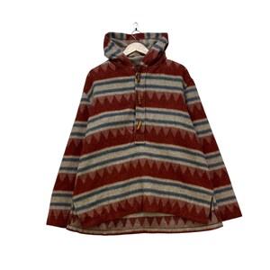 May include: A hooded pullover with a geometric pattern in red, blue, and beige stripes. The sweater has a buttoned neckline and a hood. The fabric appears to be a thick, woven material, suitable for cooler weather.