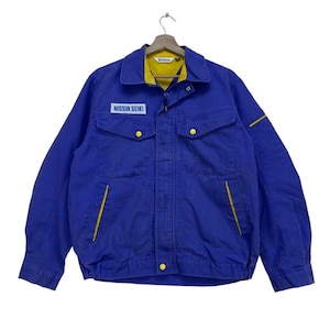 Puede incluir: Una chaqueta de trabajo azul con detalles amarillos y el texto "NISSIN SEIKI" en el pecho izquierdo.
