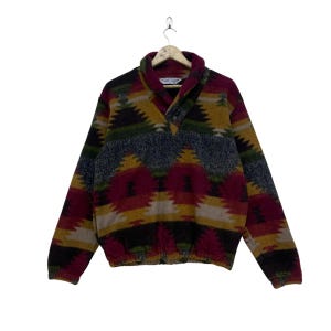 Könnte beinhalten: Vintage Fleece-Pullover mit geometrischem Muster in Burgunderrot, Gold, Grün und Grau. Das langärmlige Oberteil hat einen Kragen und einen Knopfverschluss. Der untere Saum ist elastisch. Das Kleidungsstück hängt an einem Kleiderbügel.