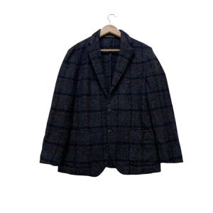 May include: A dark gray blazer with a plaid pattern, hanging on a wooden hanger. The jacket has a two-button closure and two front pockets. The plaid design features dark blue lines.