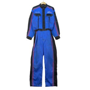 Könnte beinhalten: Blau-schwarzer Rennanzug mit roten Akzenten. Der Overall hat einen Reißverschluss vorne, mehrere Taschen und das Wort "Netz" auf der Brust. Schwarze Bahnen mit roten Streifen verlaufen an Ärmeln und Beinen. Auf einem Holzkleiderbügel aufgehängt.