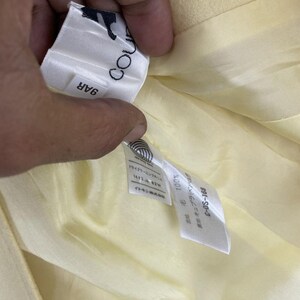 May include: Close-up of a light yellow garment's interior, revealing a tag with the text "COU" and "9AR". Additional tags display Japanese text and the numbers "100%" and "C-DS-168". The garment's lining is a similar pale yellow.