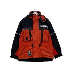 Peut inclure: Veste de ski Phenix noire et orange avec capuche. La veste comporte plusieurs poches, le nom de la marque imprimé sur la poitrine et les manches, et un petit écusson graphique. La veste est suspendue à un cintre blanc.