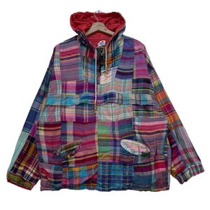 May include: A colorful patchwork jacket with a hood and a drawstring closure. The jacket features a variety of plaid patterns in shades of blue, purple, pink, and green. It has a front pocket and a red hood lining.