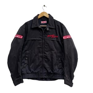 Op de afbeelding: Zwarte jas met een rood geborduurd "Simpson Racing" logo op de voorkant en "SIMPSON" patches op de mouwen.