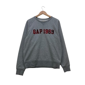 May include: A grey sweatshirt featuring the text "GAP 1969" in red. The crew neck sweatshirt has long sleeves and is displayed on a wooden hanger. The background is white.