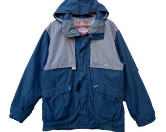 May include: A navy blue and grey hooded jacket. The jacket has a full zip, multiple pockets, and a logo patch on the chest. The hood is attached and the jacket appears to be made of a durable, weather-resistant material.