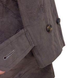 May include: A brown jacket with a buttoned cuff and two buttons on the front. The jacket is made of a soft, textured fabric.