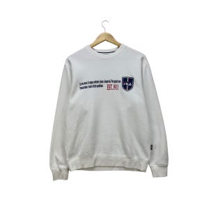 Puede incluir: Sudadera blanca con el texto "La via verso il campo centrale &egrave; dura e imperia. Per questo non trasciniamo i nostri sogni quotidiani." y un logotipo de FILA. La sudadera tiene cuello redondo y mangas largas.