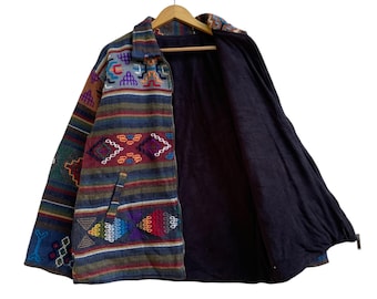 May include: A colorful, patterned jacket with a zipper closure. The jacket features a variety of geometric designs in shades of blue, green, red, and purple. The interior lining is a solid dark blue. The jacket is hanging on a wooden hanger.