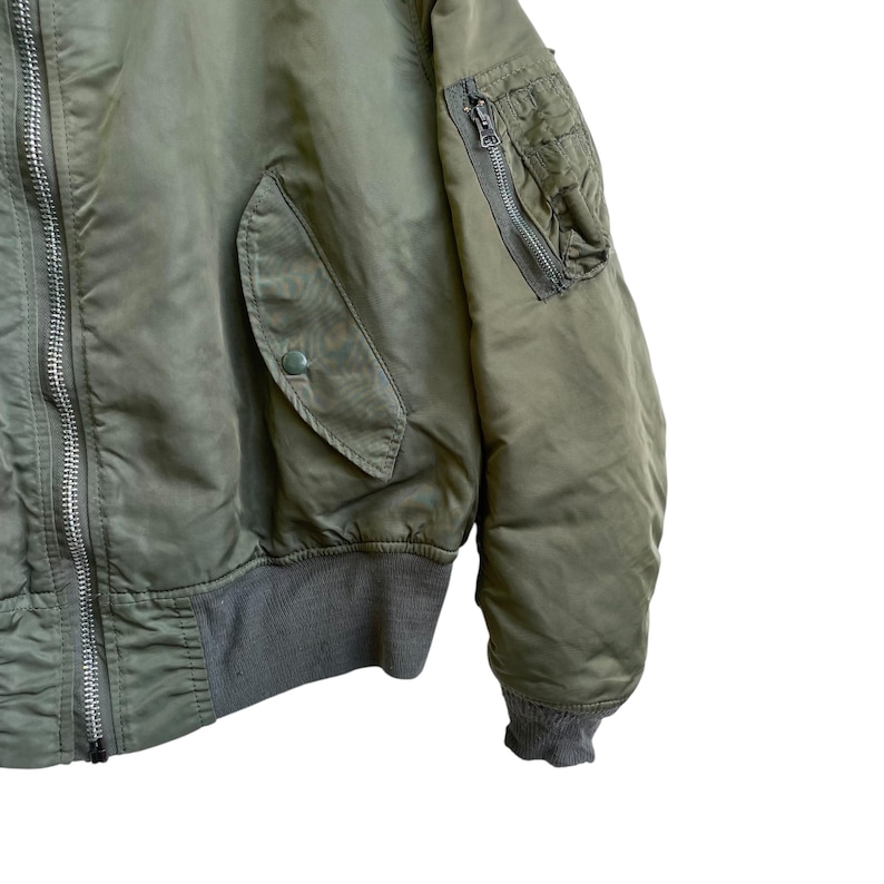 Puede incluir: Chaqueta bomber verde oliva con cuello y pu&ntilde;os de canal&eacute;. Cuenta con un bolsillo con cremallera en la manga izquierda y dos bolsillos delanteros. La chaqueta tiene cierre de cremallera plateada y cierre de bot&oacute;n en el bolsillo delantero.