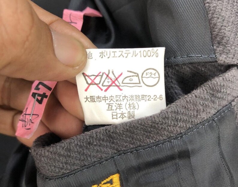 May include: A white care label with black text and symbols. The text reads "地 ポリエステル100%" "ドライ" "中" "大阪市中央区内淡路町2-2-6" "互洋(株)" "日本製".