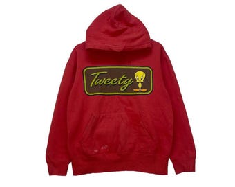 May include: Red hooded sweatshirt with a Tweety Bird graphic in a brown rectangle with yellow lettering. The graphic says "Tweety" and features a cartoon of Tweety Bird.